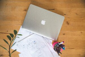 Top view of a laptop, papers, and pens on a wooden table in an office setting.
